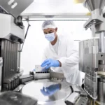 Pharmaceutical technician in a protective clothing equipment seen in a laboratory during a manufacturing process