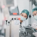 Both male and female Asian scientists are outfitted with protective gear. Examining the factory's machinery and materials used in the mask-making process. Covid 19 is a piece of preventive equipment.