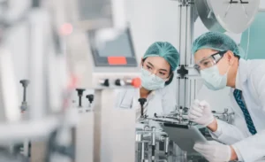 Both male and female Asian scientists are outfitted with protective gear. Examining the factory's machinery and materials used in the mask-making process. Covid 19 is a piece of preventive equipment.