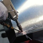 Spot welding sheet metal with precision tool. Close-up of a worker using a spot welding machine to fuse sheet metal parts with sparks flying in an industrial setting.